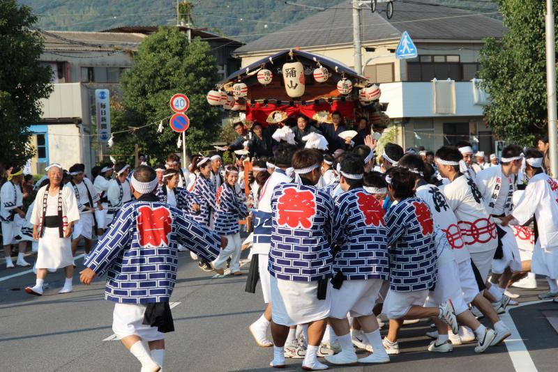 祭の文字が書かれた半被を着た人たちがお神輿を担いでいる写真