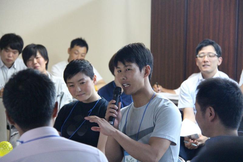 室内で座ってマイクを持って話す男性と座って聞く若者たちの写真