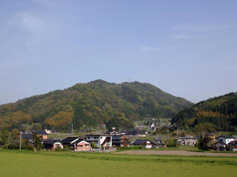 青空にうっすらと雲がかかった天候の日に撮影した山のふもとの民家の写真