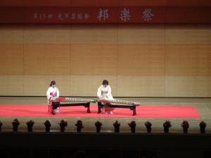 舞台に着物を着た女性が2人並んで座っていて、それぞれ琴を演奏している写真