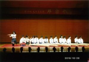 舞台の上で笛を吹く女子学生と三味線を演奏する2人の女子学生と琴を演奏する11人の女子学生の写真