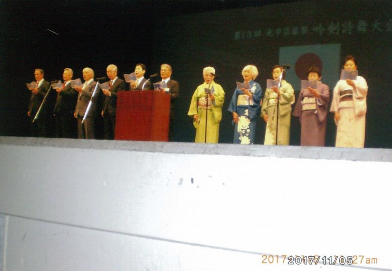 舞台上で一列になって吟詠を披露する11人の男女の写真