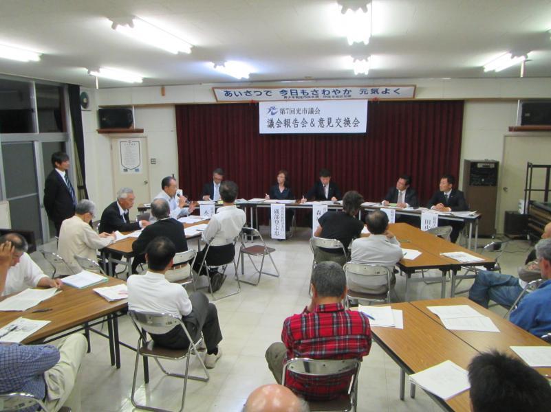 5名の議員などと向かい合い、会議テーブルで4つの島を作り資料を読み込む参加者の写真