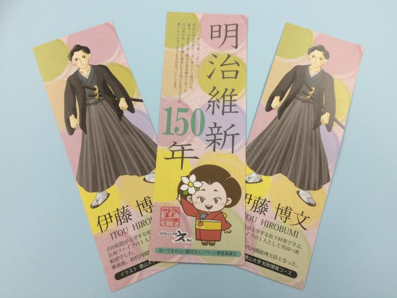 明治維新150年という文字と着物をきた女の子のイラストがかかれたしおりの両脇に伊藤博文の全身のイラストが描かれたしおりが並べてある写真