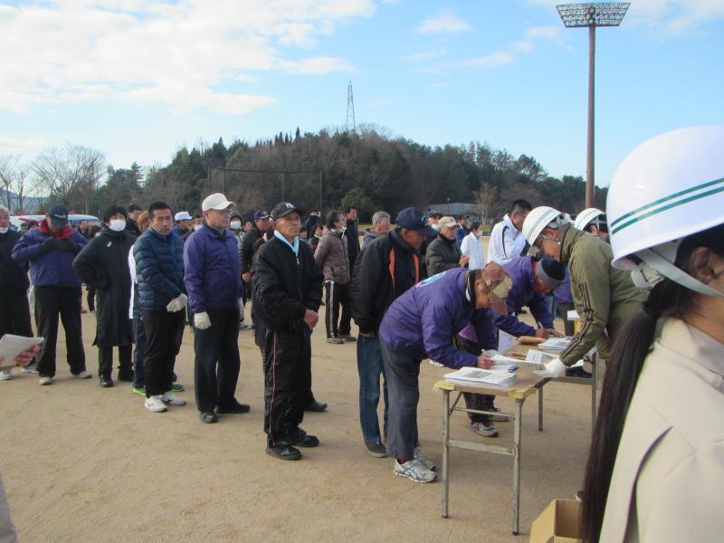 広場で防災訓練の受付をするために列になって並んでいる人々の写真