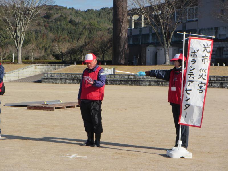 光市災害ボランティアセンターの旗と指し棒を持つ女性と指し棒で差されたゴーグルを見る男性の写真