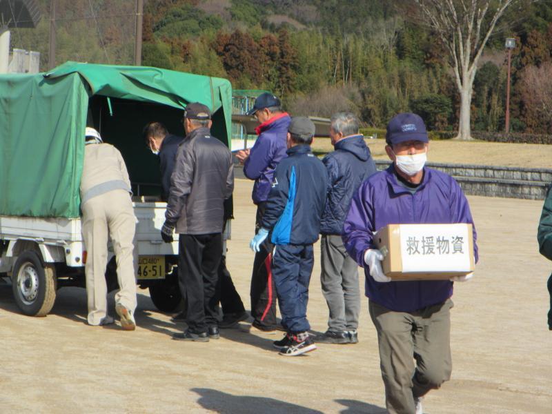 トラックの後ろに並びながら救援物資を受け取る六人の人々と救援物資を運ぶ一人の男性の写真