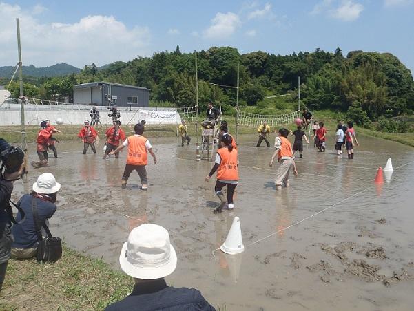 オレンジのゼッケンをつけているチームと赤いジャンパーを着ているチームに分かれてどろんこバレーの試合をしている写真