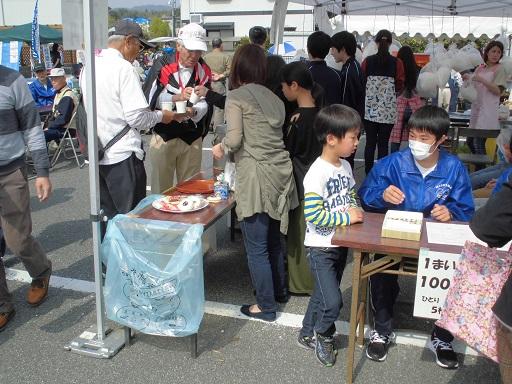 テントの中で飲み物が振舞われたり、綿菓子が販売されたり、青いスタッフジャンパーを着た学生が男の子と話をしている写真