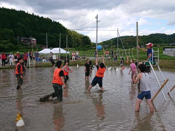 田んぼ中でどろんこになりながらバレーの試合が行われている写真