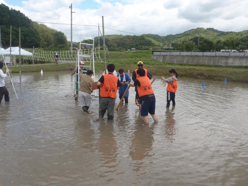 地域ふれあい協働隊員らが田んぼのどろんこの中にバレーコートを設営している写真