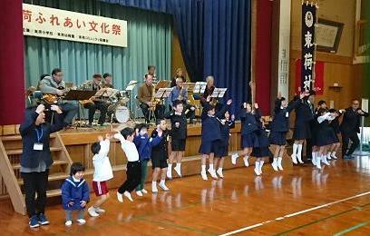 束荷ふれあい文化祭で、舞台上で演奏する高齢の男女と、舞台下で、飛び跳ねる子供たちの写真