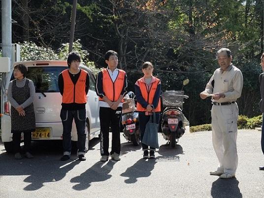 オレンジ色のベストを着て立っている3人の地域ふれあい協働隊とそばに立っている男性と女性の写真