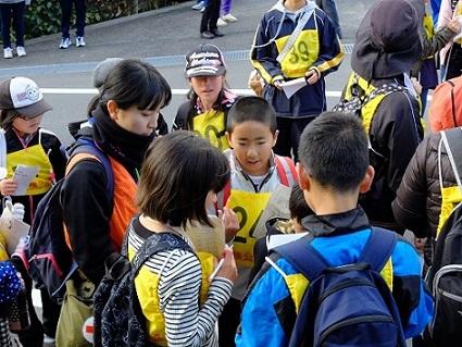 参加している子供たちが紙と鉛筆を持って考え事をしているのを見守っている女性隊員の写真