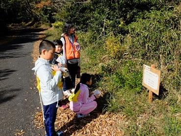 女性隊員と参加している子供たちがコースの途中で紙を見ながらあぜ道にある看板をみて考え事をしている写真