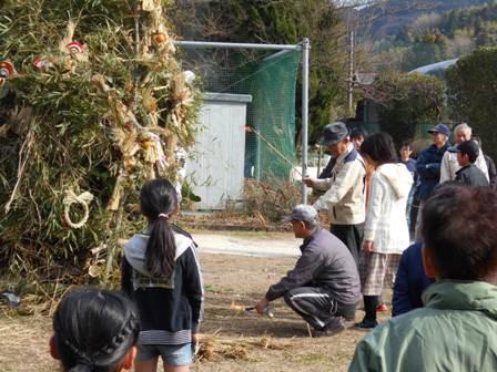 外に置いてある竹で組まれたヤグラに点火される様子を人々が見ている写真