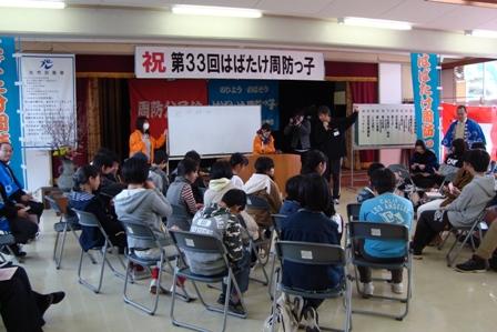 公民館の室内で小学校6年生、中学校3年生の卒業生が椅子に座って話を聞いている写真