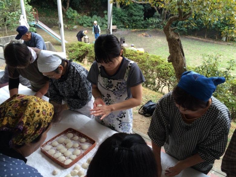 公民館でエプロン姿の女性たちが餅を丸めている写真