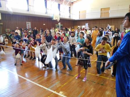 ロープが張られた線の後ろに集まった子供たちが、袋を持ち両手を上にあげ笑顔で写っている写真