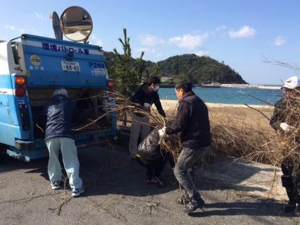 撤去した枯れた植物をパッカー車へ男性たちが運んでいる写真