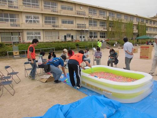 グラウンドに水風船が入った簡易プールが設置されている場所で競技の準備をしている隊員の方々の写真