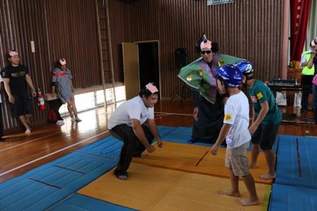 体育館でマットの上に敷かれたござの上で相撲を取ろうとしている写真