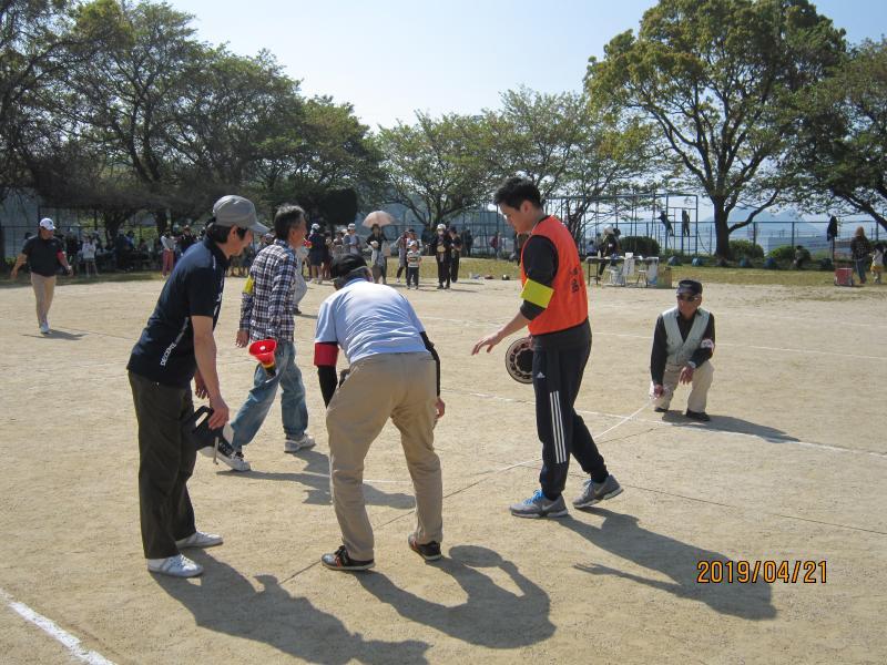 グラウンドでゴム長靴が飛んだ距離をメジャーで測っている男性隊員の写真