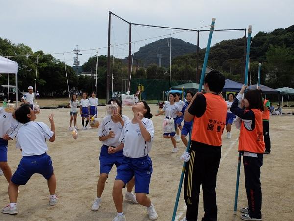 グラウンドで体操服を着た中学生たちがパン食い競争をしている棒を隊員が支えている写真