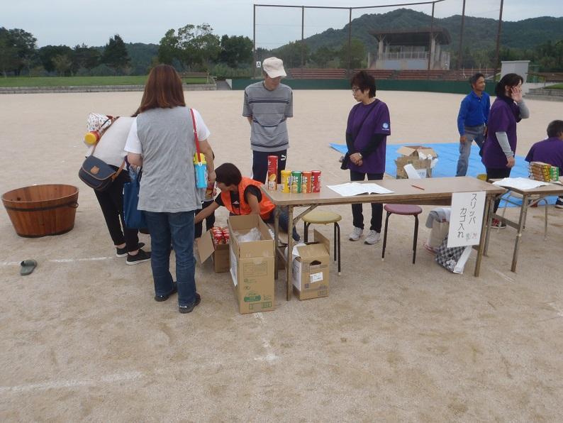 受付のテーブルの横で女性隊員が座って参加者の対応をしているのを母親や男性スタッフが見ている写真