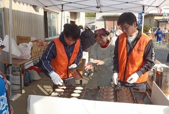 テントの中で隊員の方がたい焼きを作っていて、その横で係の人が教えている写真