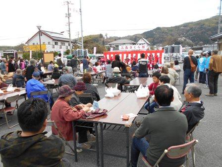 紅白幕のかけられた三島さくら祭のステージでの催し物を椅子に座って見ている人々の写真