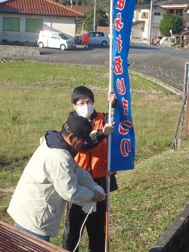 道路沿いに塩田ふれあいまつりののぼり旗を設置している男性2名の写真