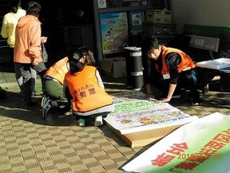 ロビーで隊員が縦長の板に看板の紙を張っている写真