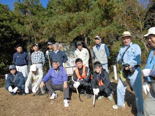 鎌や草刈り機を持った男性たちがきれいになった山道で記念撮影している写真