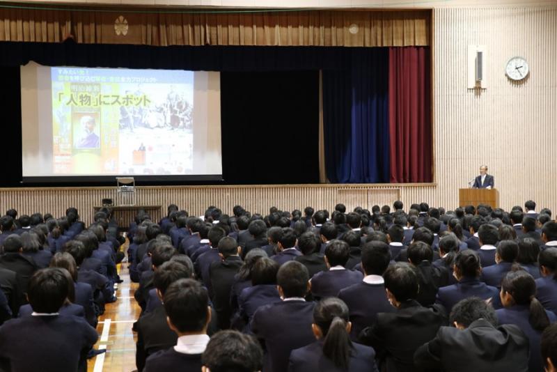 スクリーンに映像が映し出されている中、座って講話を聴く学生たちの写真