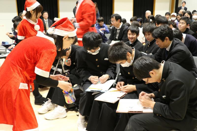 サンタクロースのコスチュームを着た女性スタッフが学生のオーナメント作りを手伝っている写真