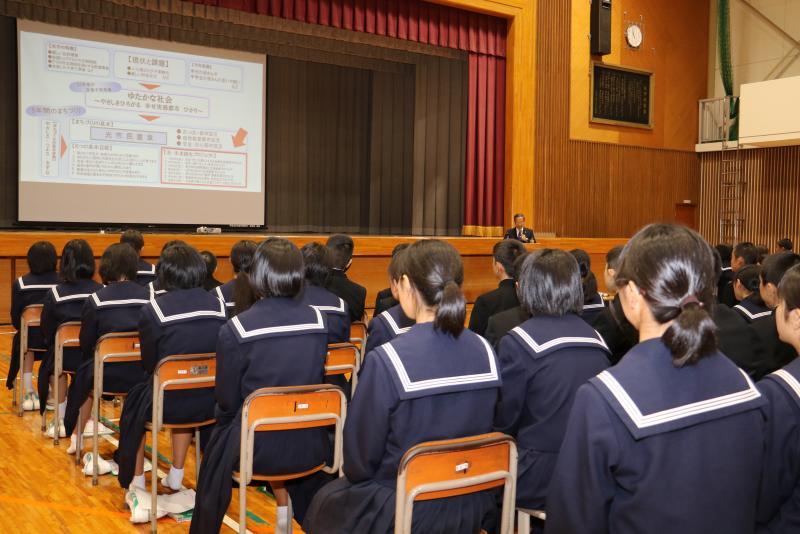 体育館で制服を来た学生たちが並んで着席している写真