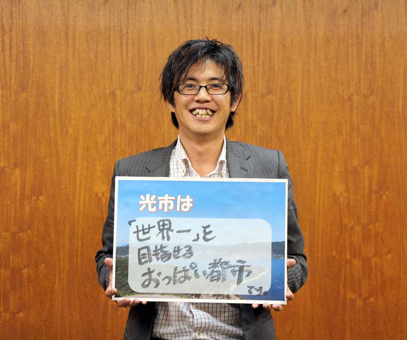 「光市は『世界一』を目指せるおっぱい都市!!」のパネルを持つ佐々木さん