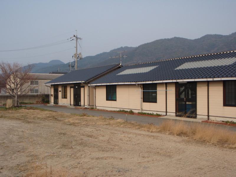 背景に山がある黒い瓦屋根が特徴的な横長の建物の写真