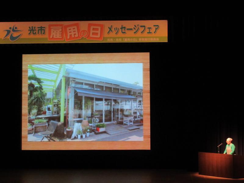 ステージ上のスクリーンに店舗の外観が映し出されている写真