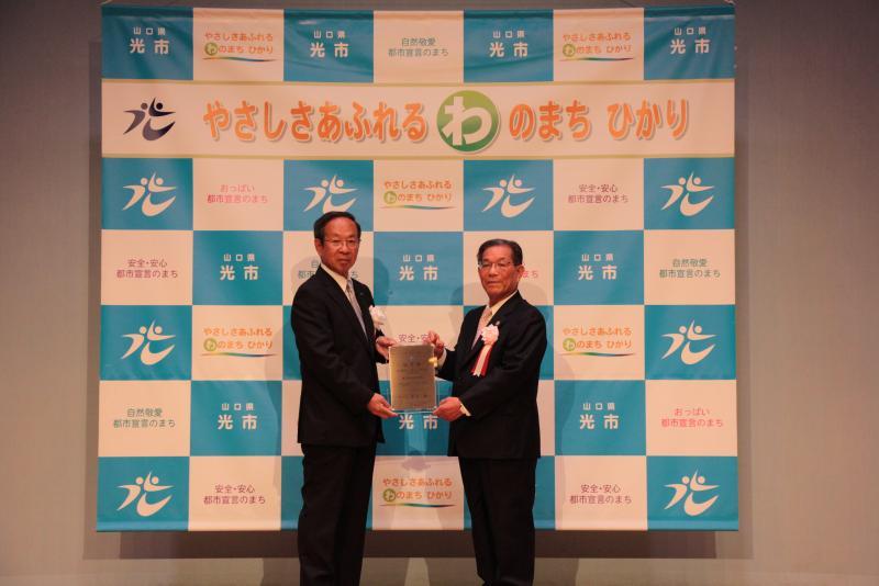室内で一緒に認定盾を持って映る二人の男性の写真