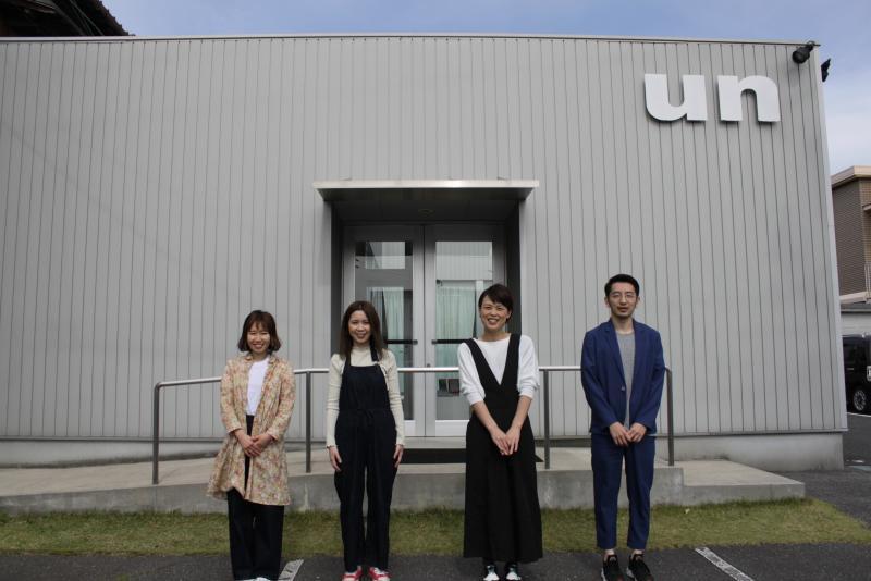事業所の前で従業員が笑顔で横一列になって並んでいる写真