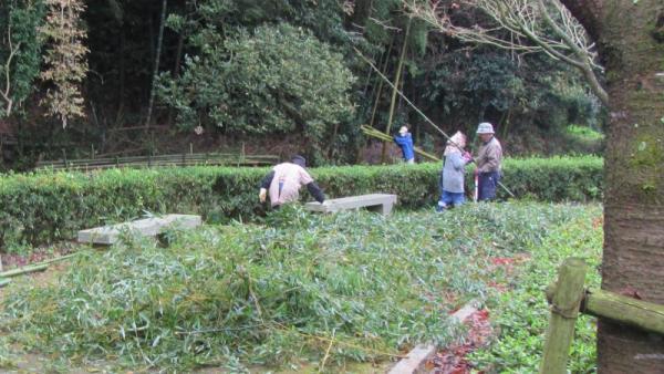 草刈りで出た大量の雑草とその奥にいる4人の男女の写真