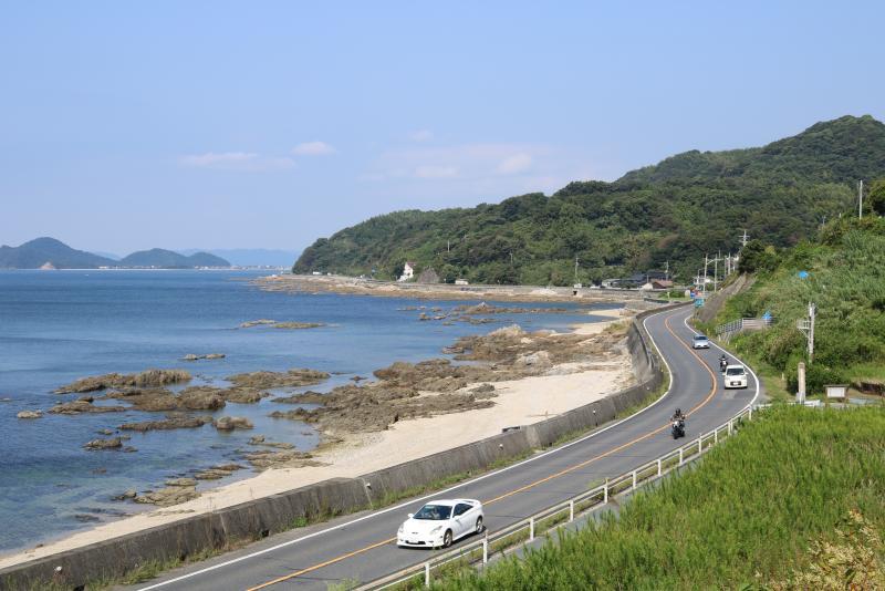 海辺の砂浜の隣にある一本道の道路を車両が走っている写真