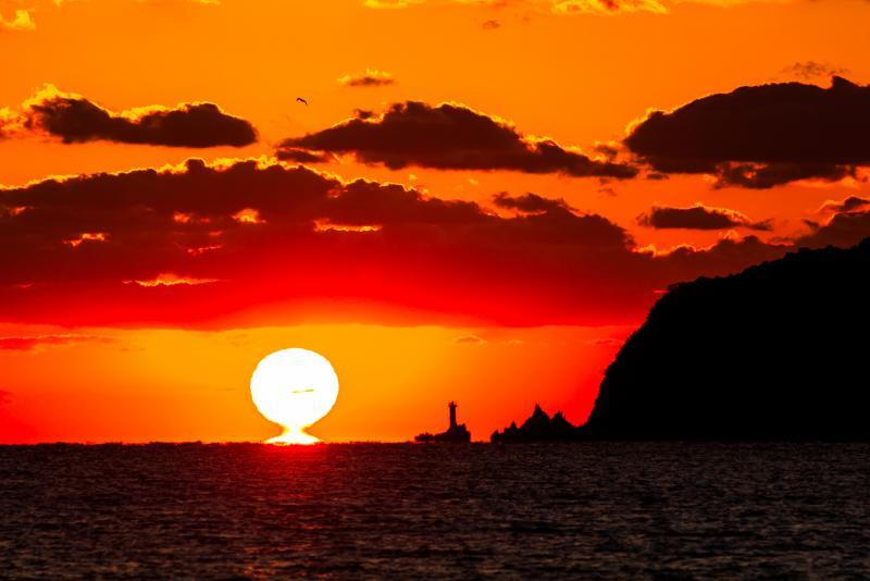 海の向こうの水平線に太陽が沈んでいく写真