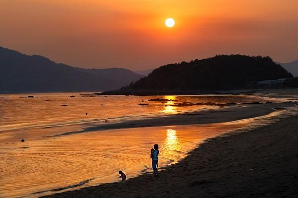 夕暮れに赤く染まった空とその光が反射した海岸にいる人物の写真