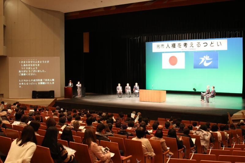 「光市人権を考えるつどい」と書かれた横断幕のあるステージと客席の写真