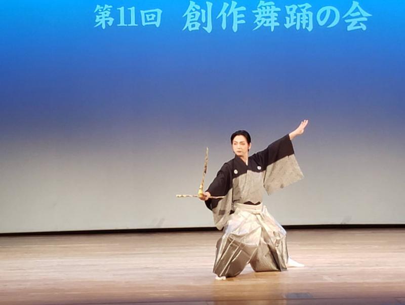 舞台上で着物を着た人が大きな折り紙の鶴を手に持って踊っている写真