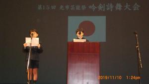 舞台の上に二人の男の子が立っていて原稿用紙を見ながら話をしている写真