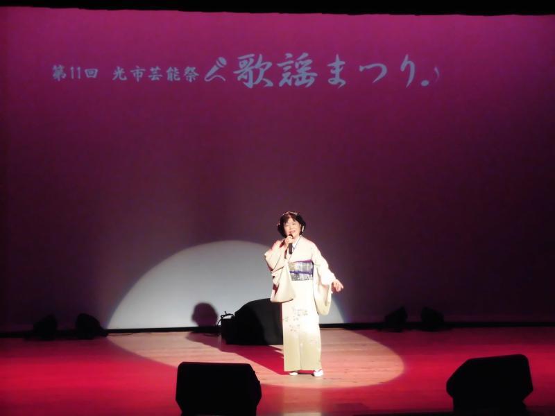 舞台の上で白い着物を着て歌を歌っている女性の写真